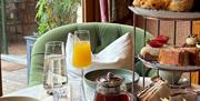 A table of afternoon tea with champagne and bucks fizz in a flutes next to a large garden glass door.