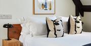 A neatly made bed with white linens, two pillows featuring abstract black and white faces, a wooden bedside table with a black lamp, and framed modern