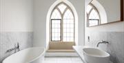 Minimalist bathroom with a freestanding bathtub, oval sink, large arched window with a stone bench, marble walls and floors, and a rectangular mirror