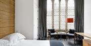 Minimalist hotel room with a large Gothic-style arched window, sheer curtains, two modern chairs, a round coffee table, a red floor lamp, wooden wall