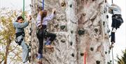 Three children attached to ropes and harnesses scaling a climbing wall