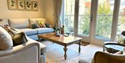 A bright, naturally lit living room with grey sofas overlooking a balcony through glass doors.