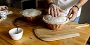 A closeup of two pies being prepared by a person wearing a chef's coat.