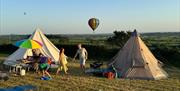 Two bell tents pitched in a field at Bucklegrove Holiday Park, with two hot air balloons flying in the background