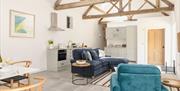 An interior living area with a blue sofa and armchair, stone floors and a high ceiling with wooden beams.