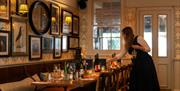 A waitress placing a glass on a long table at The crstal Palace. The table is placed alongside a wall covered in many framed images and a round mirror