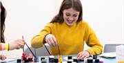 A girl wearing a bright yellow jumper creating an artwork with coloured inks
