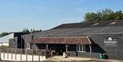 Outside barn building made of black wood and with a Flourish white sign, and parking outside.