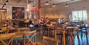 A cafe with lots of wooden tables and chairs and hanging ceiling lights