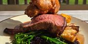 A plate of roast beef, vegetables, and a large Yorkshire pudding on top - on an outside wooden table.