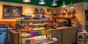 A wooden cafe counter with drinks and sandwiches on show, and hanging ceiling lamps.