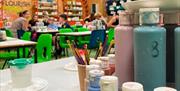 Paints on a table with childing sitting in the background crafting