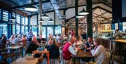 Indoor farm shop cafe with dark ceiling beams, hanging lights and wooden table and chairs