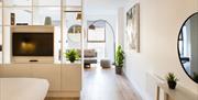 A bright living area with lots of natural lighting, white walls and shelving, a TV and several potted plants.