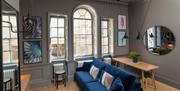 A modern living room with a blue sofa, two large wall mirrors, grey walls and large windows.