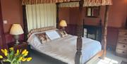 A bedroom with a wooden four poster bed with short frill curtains around the top and full length white fabric at the head of the bed.
