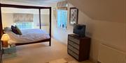 A stylish attic bedroom with cream carpet, a black modern four poster bed with white sheets and two dark coloured cushions on it.