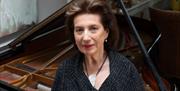 A woman standing in front of a piano and looking towards the camera.