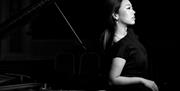 A woman leaning against a piano looking away from the camera.