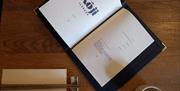 A nicely branded Koji menu book open on a page with it's logo, along with chopsticks, a napkin and cup