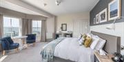 A room in the Lansdown Grove Hotel with a large bed, a small table and two chairs. Large windows on the wall opposite the bed show a view of a scenic