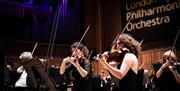 Orchestra performers playing on a stage in front of a banner with the words 'London Philharmonic Orchestra' written on it.