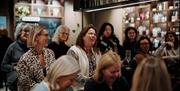 A group of women at an event sat on chairs all facing the same direction, inside of Molton Brown's store in Bath.