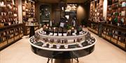 A luxurious store interior, with ceiling-high shelves on either side of the room and a circular unit in the centre all displaying bottled products