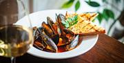 A plate of mussels and garlic bread with a glass of white wine.