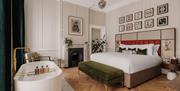 Highly spec'ed bedroom with oak parquet flooring, a green velvet ottoman and free standing bath at the end of a double bed with a Victorian fireplace.