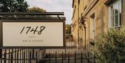 A hanging sign saying '1748' Bar and Lounge in italic font outside a Georgian row of sandstone buildings