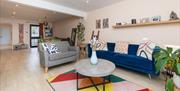 An open-planned living room space with a blue sofa, grey love seat, round coffee table and geometric multi-coloured rug.