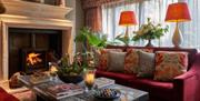 A living room space with velvet claret sofas covered in patterned cushions, and a fireplace behind.