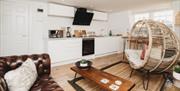 A combined living room and kitchen space with a brown leather sofa, wooden coffee table and woven egg chair.