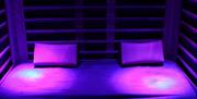 A bench with two cushions inside an infrared sauna room with purple light.