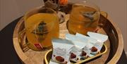 Two cups of tea steeping in glass mugs, and a row of Lindt "choco wafer" treats, on a circular wooden tray.