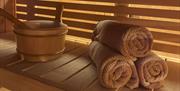 Three rolled-up towels stacked on a light wooden shelf, alongside a circular wooden pot.
