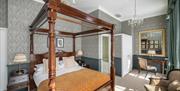A Georgian style elegant bedroom with a wooden four poster bed in it and a desk with chairs.