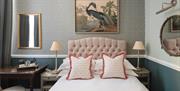 A Georgian style bedroom with pink and grey tones and a picture of an elegant exotic bird above a double bed.