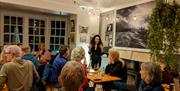 A lady (Simi) teaching a cookery class to a room of people at a restaurant listening