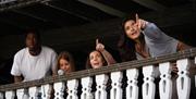 Four people stand on a balcony; two are pointing off into the distance.