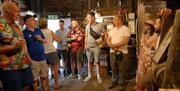 Tour group stood watching a guide inside a building with wooden walls on the Somerset Cider and Cheese Experience.