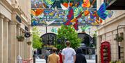 Pedestrians walk beneath large, multi-coloured model butterflies suspended above the high street.