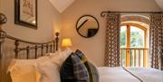 A guest bedroom with wrought iron double bed, tartan style cushions, a picture and circular mirror on the wall, and a small wooden balcony with curtai