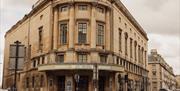 The exterior of The Forum, a large building made of distinctive yellow Bath stone. The entrance is built into a curved corner of the building.