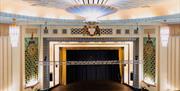 Image taken from the balcony shows an unobstructed view of the stage at The Forum, with ornate decorations on the surrounding walls and ceiling.
