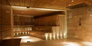 A large glass fronted sauna with wooden staged steps to sit on and low warm uplighters.