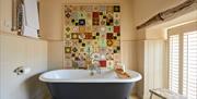 A free standing grey bathtub with a wooden tray across it. In the background a colourful tapesty hangs from the wall