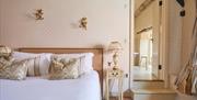 A light coloured bedroom with a bed with white sheets and small bedside table to the right of the bed. A lamp rests atop of the table