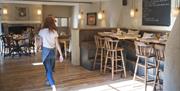 A person wearing blue jeans and a white t-shirt walking through a room that has wooden tables and stools